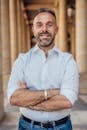 Confident man standing with crossed arms in a historic Parisian arcade, exuding professionalism and style.
